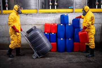 Workers in chemicals production factory moving barrels and canisters with acid or dangerous...