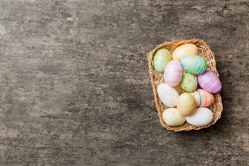 Colorful Easter eggs in wicker basket against colored background, closeup. top view with copy space