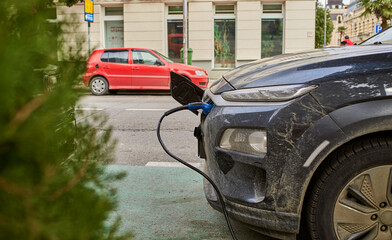 An electrical car on the street with the inserted charger is charging