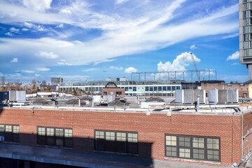 Exterior facade of a two storey red brick industrial factory building showing windows and blinds, rooftop with vents, skylights and air conditioners, blue sky with clouds, nobody