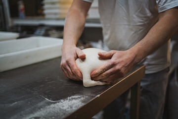 Anonymous baker man kneading bread dough on metal table in a bakery