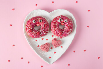 Two bright pink donuts in a heart-shaped plate on pink background, the idea of a romantic breakfast for Valentine's Day, Top view