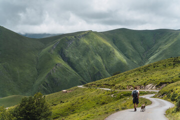 young man hiking on a trail with his dog with large green mountains in the background