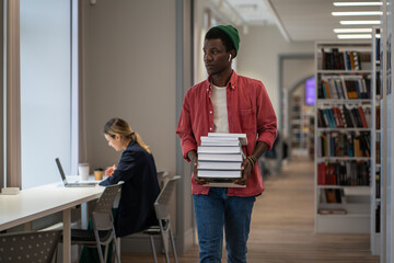 Pondered African American guy student borrowed books from library to effectively study at university and receive scholarship. Quality education starts with reading. Pensive man with stack of textbooks