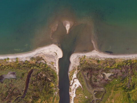A topdown aerial view of the point where a river meets the sea