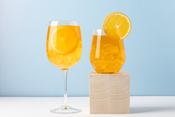 Orange drink with ice in glass on blue background. Refreshing tropical summer fruit lemonade or alcoholic drink with orange slice