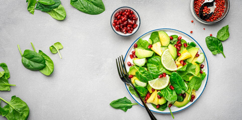 Avocado vegan salad with pineapple, spinach and pomegranate seeds, gray table, top view. Healthy eating, clean food, diet, weight loss concept. Banner