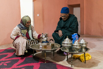 Berber man and woman with traditional clothes in the living room of their house preparing tea for...