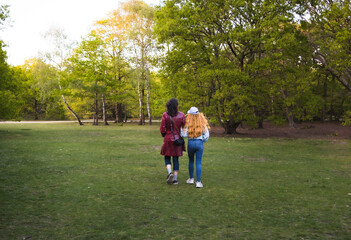 Naklejka premium Middle-aged woman and her teenage daughter walking on footpath in park in spring at sunset