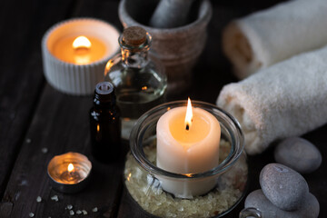 Spa setting with essential oil, candle, sea salt, pebbles, towel on dark wooden background. Massage, aromatherapy. Natural organic ingredients for relaxation, detention. Wellness in salon concept