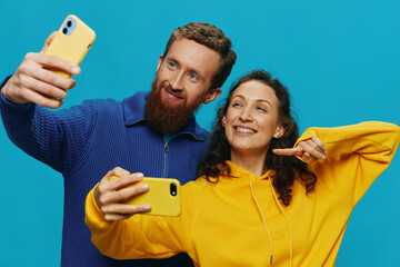 Woman and man funny couple with phones in hand taking selfies crooked smile fun, on blue...