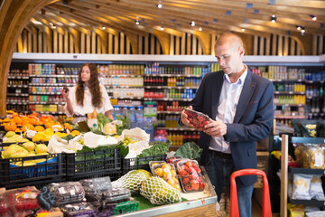 Obraz premium Man chooses and buys strawberry in a grocery supermarket
