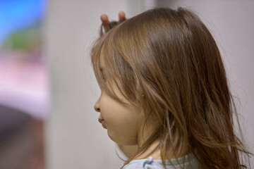 Fototapeta premium A little girl holds a blush brush to apply powder on her cheeks and face, happily looking in the mirror. Cute baby is playing makeup makeup game..