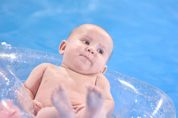 A small child aged 6 months swims in the pool, swims on a balloon, mom helps him stay in the balloon.