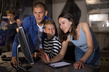 Cheerful young parents with two sons spending funny time in quest room decorated as lost underground shelter using computer to find solution to puzzle