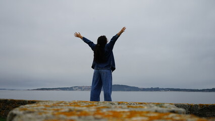 Woman on his back with the sea in the background raising his arms happily