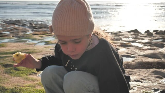 Girl at the beach playing with water while eating an apple