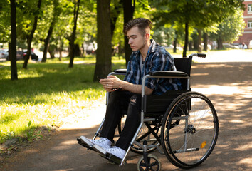 young disabled man in wheelchair walking park and listening music
