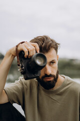 Obraz premium a young man with a modern SLR camera in his hands on a natural background