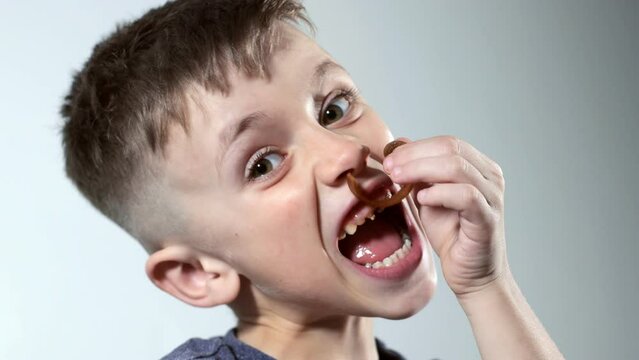 A little boy opening sweets and taking pastila his mouth while sitting on a cozy sofa. A child enjoys candy