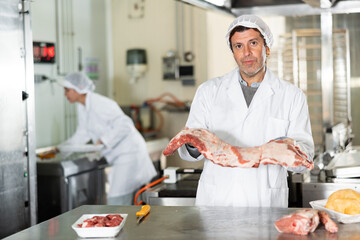 Male kitchen worker closely examines raw meat for cutting and preparing for sale