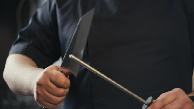 Slow motion close-up video of a chef sharpening a knife in the kitchen. A professional prepares knives for slicing food to prepare meals for restaurant visitors.