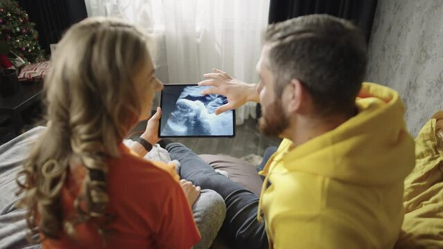 Pregnant couple in love looking at baby photo on tablet. A family is expecting a child. A man and a woman look at the ultrasound diagnosis of the fetus.