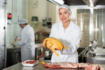 Female kitchen worker with raw chicken carcass in her hands and raw meat prepared for sale