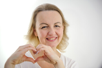 woman sincerely smiles with hands shows a heart squinting her eyes on a white background love feelings joy valentine's day like goods product delivery advertising space we I love it love you