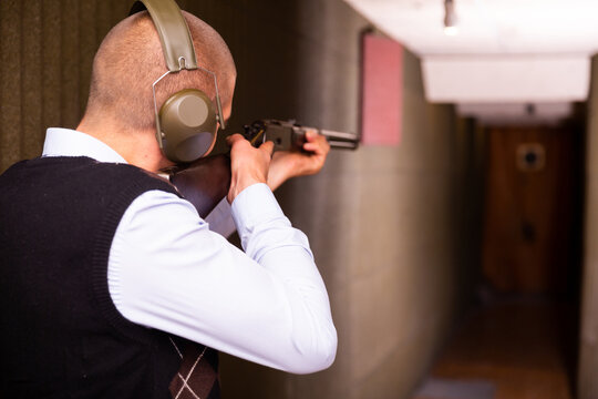 Rear view of man wearing protective earmuffs practicing shotgun shooting at target at shooting range