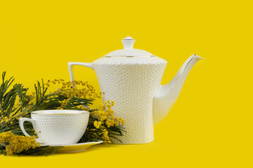Side View White Teapot and Floral Elegance. White teapot and cup with yellow mimosa on a vibrant...