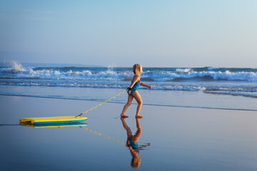 Little baby girl - young surfer with bodyboard has fun on sea beach. Family lifestyle, people...