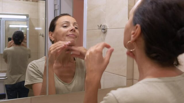 Aging woman. A lovely woman looks at her aging face in the bathroom mirror.