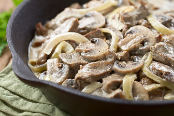 Fresh homemade creamy beef stroganoff with mushroom slices and onion in cast-iron skillet (Selective Focus, Focus in the middle of the image)