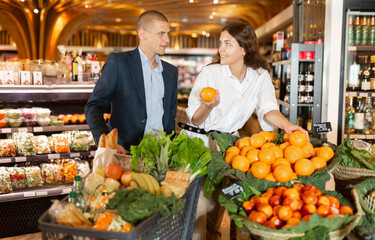 Portrait of young woman and man doing shopping at vegetables department at supermarket