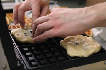 Close-up chef pours waffle batter in a waffle iron in a professional kitchen. Waffle making at the hotel with all-inclusive meals. belgian waffles in a waffle iron.