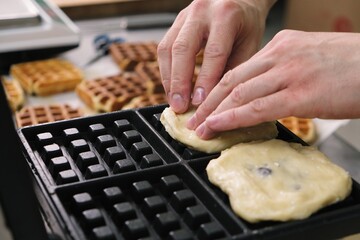 Close-up chef pours waffle batter in a waffle iron in a professional kitchen. Waffle making at the hotel with all-inclusive meals. belgian waffles in a waffle iron.