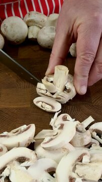 Chefs hands slicing button mushrooms with knife.