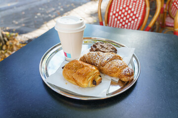 Delicious French breakfast served on metal plate consist of fresh croissant, Pain au chocolat and chocolate cookie. Selective focus on Almond Croissant crust 