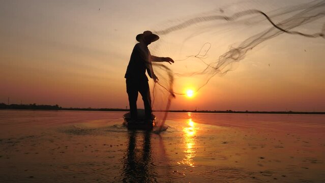4K Slow Motion, silhouette of fisherman throwing fishing net during sunrise on boats at the lake. Traditional culture of Thailand. Fisherman's life style.