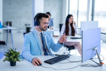 Handsome male operator with headset in blue suit working on computer in call center.