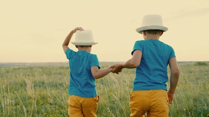 Naklejka na ściany i meble Children, friends, travel to summer field holding hands. Children's dreams and fantasies in outdoors. Boys play in park in summer at sunset. Carefree children play together outdoors. Happy family