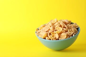 Bowl of tasty crispy corn flakes on yellow background, space for text