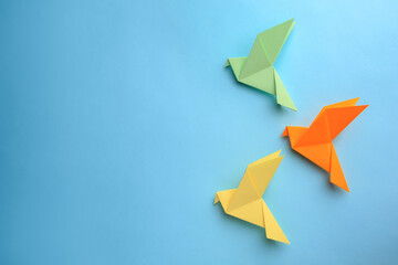 Origami art. Colorful handmade paper birds on light blue background, flat lay. Space for text
