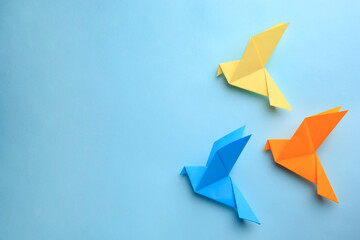 Origami art. Colorful handmade paper birds on light blue background, flat lay. Space for text