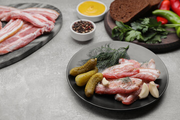 Tasty pork fatback, pickled cucumbers and ingredients on grey table