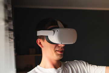 A young guy is wearing virtual reality or oculus head set and playing in virtual reality in his room