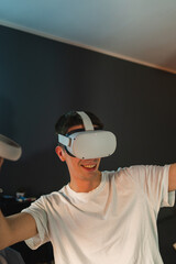 A young guy is wearing virtual reality or oculus head set and playing in virtual reality in his room