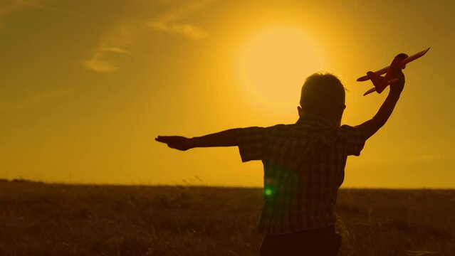 Teenager dreams of flying, becoming pilot. Dream travel. Happy child boy runs with toy airplane on field in sunset light. Boy wants to become pilot astronaut. Slow motion. Children play toy airplane.