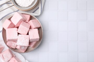 Bowl of delicious sweet marshmallows with powdered sugar on white table, flat lay. Space for text